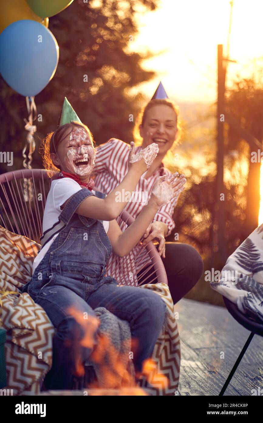 Mother and daughter duo celebrating the daughter's birthday. Laughter fills the air as they delight in the daughter's face covered in sweet, creamy fr Stock Photo