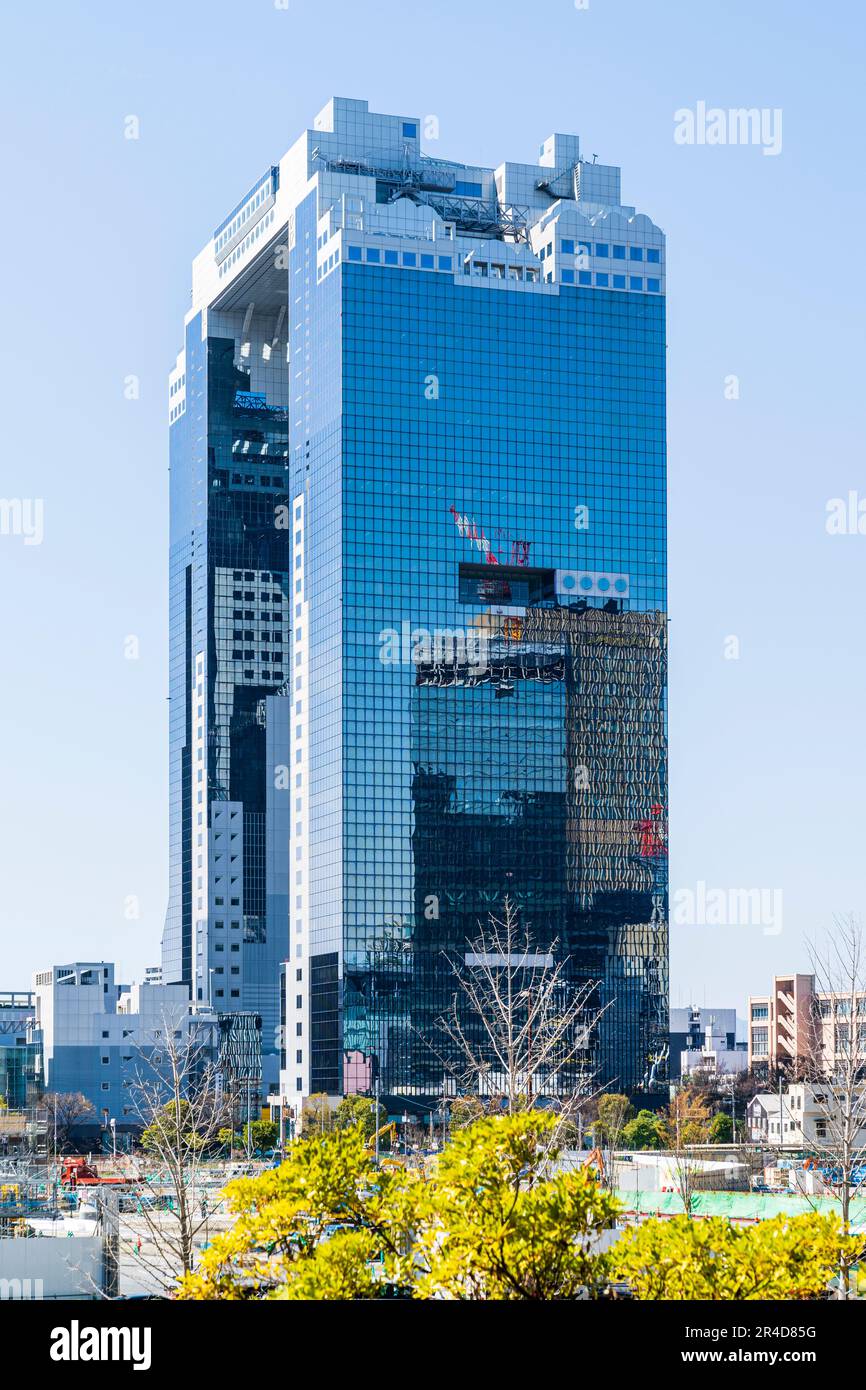 The landmark Umeda Sky Building on a sunny day in the spring with clear blue sky behind. Another office blocks with cranes on reflected in the facade. Stock Photo