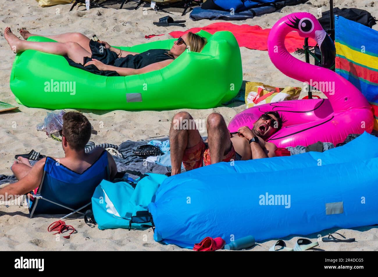 St Ives, UK. 27th May, 2023. Sleeping on a pink flamingo - People flock to the beach to sunbathe as well as take part in watersports and boat trips - Sunny weather for the bank holiday weekend in St Ives. Credit: Guy Bell/Alamy Live News Stock Photo