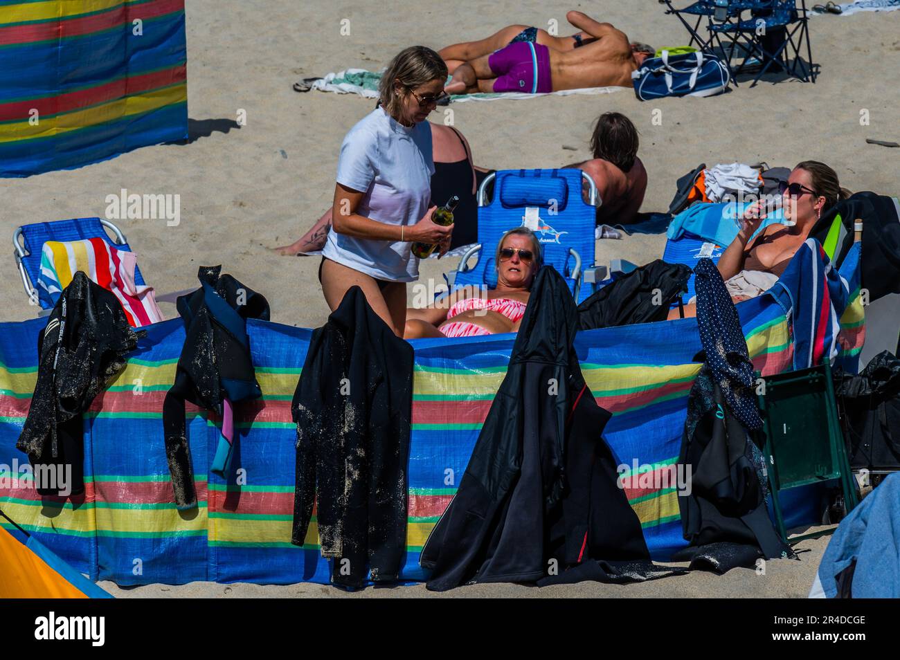 St Ives, UK. 27th May, 2023. Wetsuits hang out to dry on a windbreak - People flock to the beach to sunbathe as well as take part in watersports and boat trips - Sunny weather for the bank holiday weekend in St Ives. Credit: Guy Bell/Alamy Live News Stock Photo