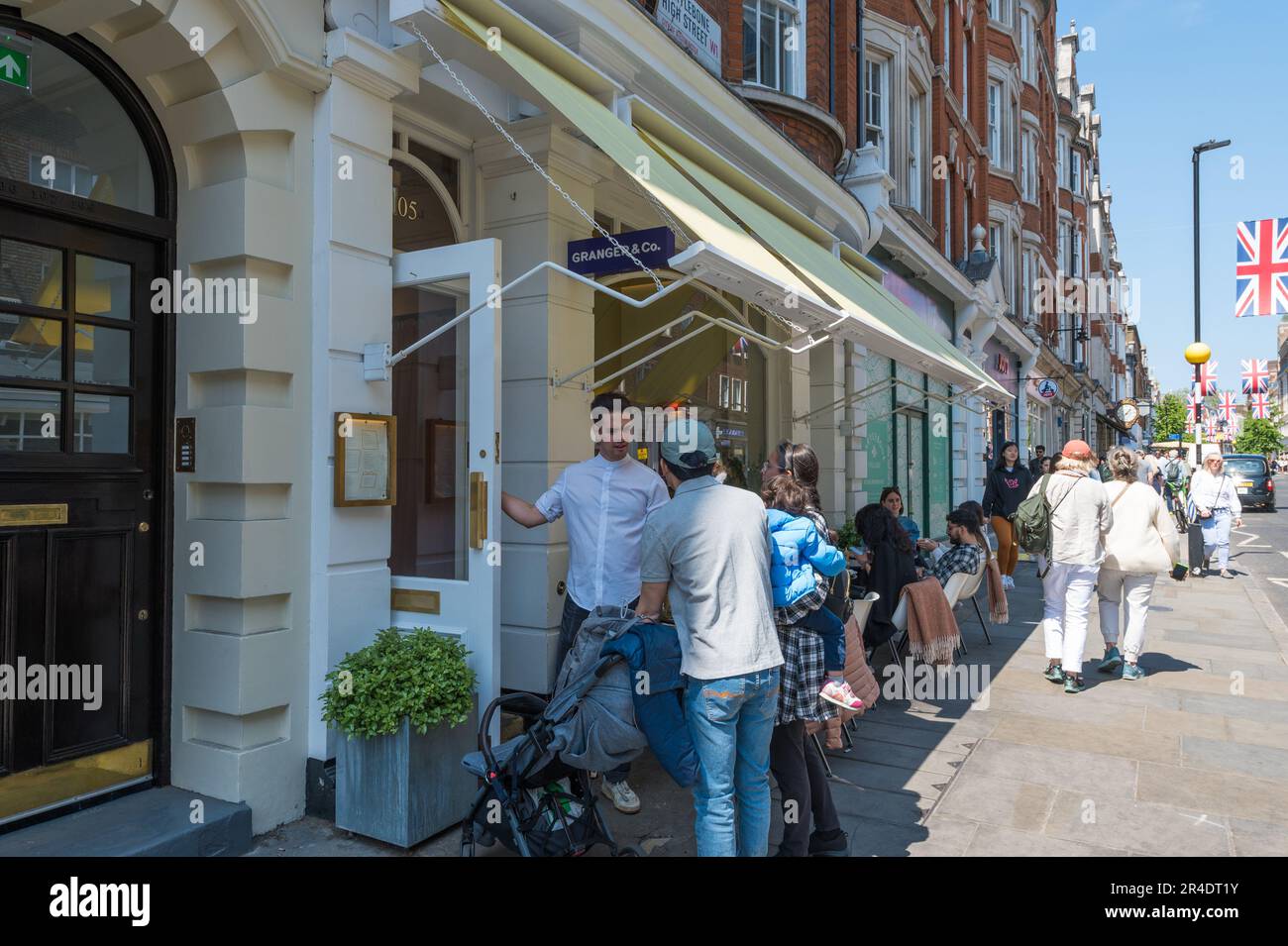 Waiter greets customers at the entrance to Granger & Co. restaurant on Marylebone High Street, London, England, UK Stock Photo