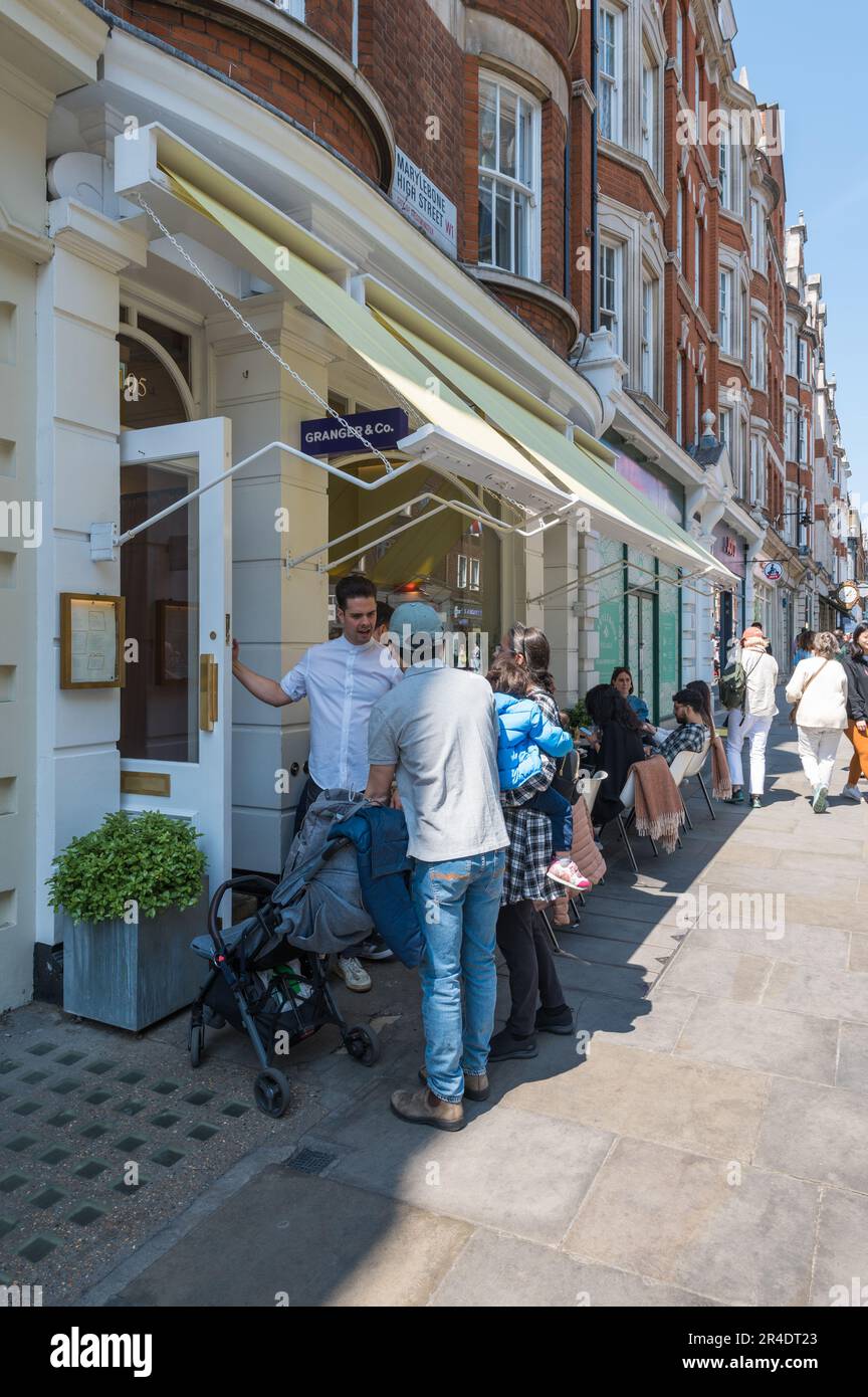 Waiter greets customers at the entrance to Granger & Co. restaurant on Marylebone High Street, London, England, UK Stock Photo