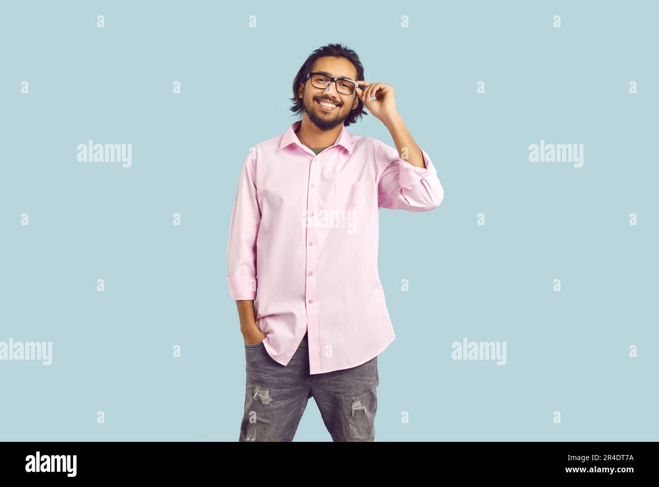 Young casual bearded Indian man student smiling adjusts glasses stands on turquoise background Stock Photo
