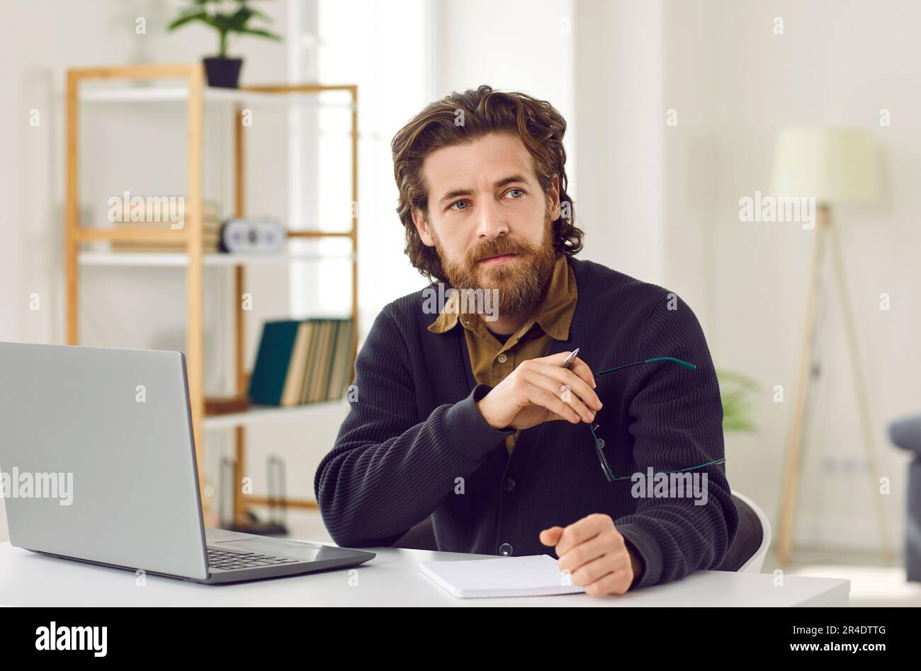 Serious pensive businessman who works with laptop and notepad thinking about solving work problem. Stock Photo
