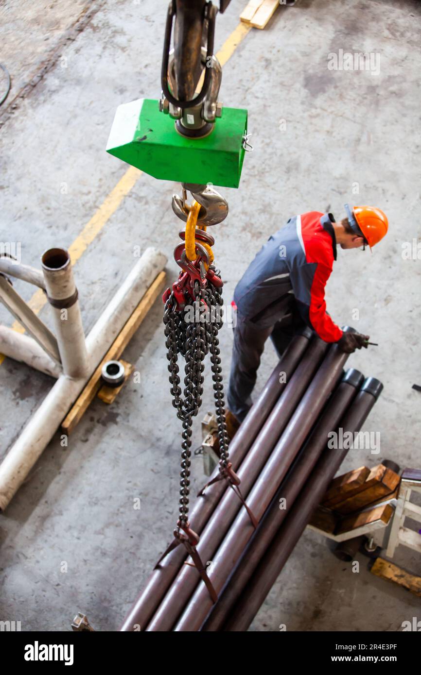 Worker preparing steel pipes to lifting. Chain in focus only. Low depth of field Stock Photo