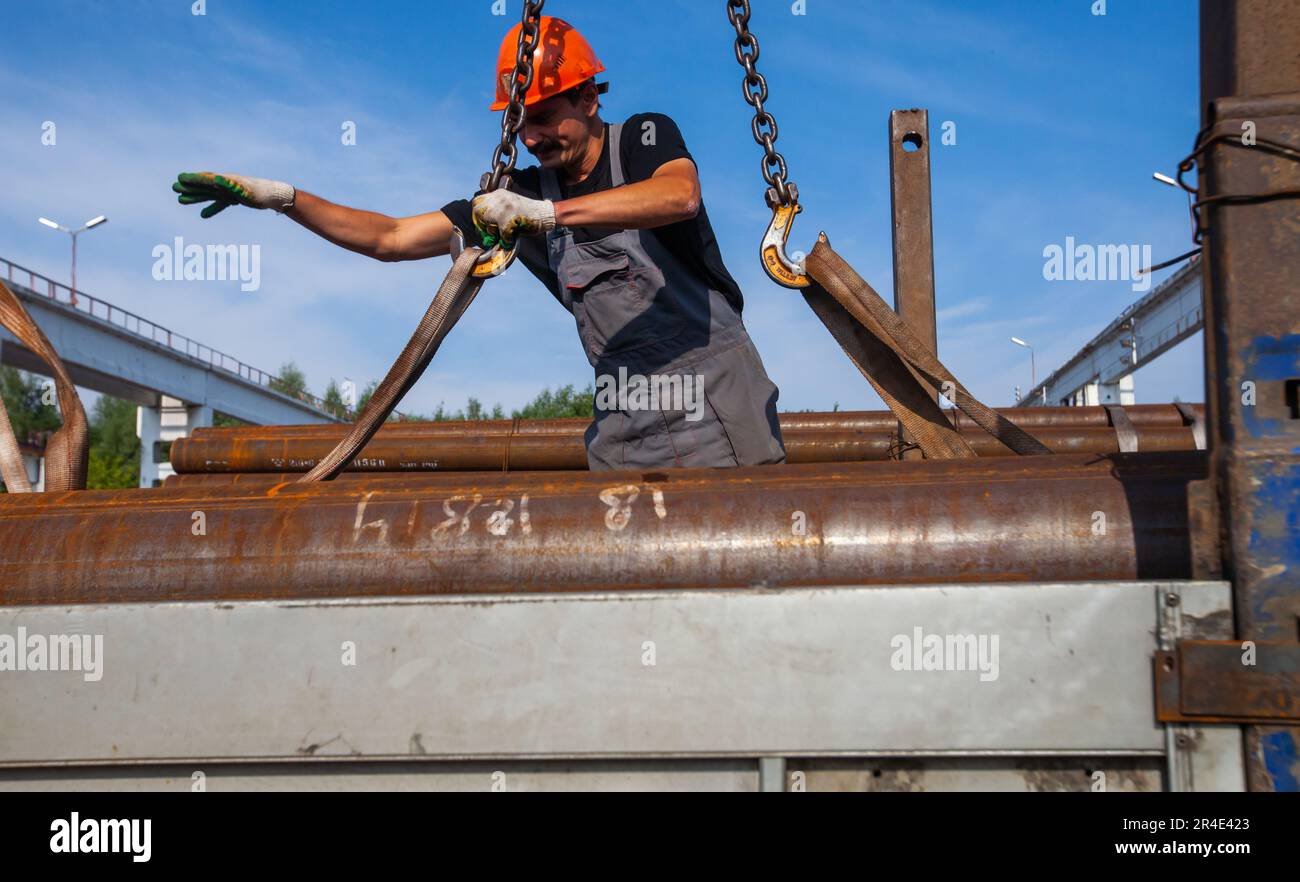 Podolsk, Moscow province - August 02, 2021: Pipes warehouse. Worker loads pipes with overhead crane and straps. Stock Photo