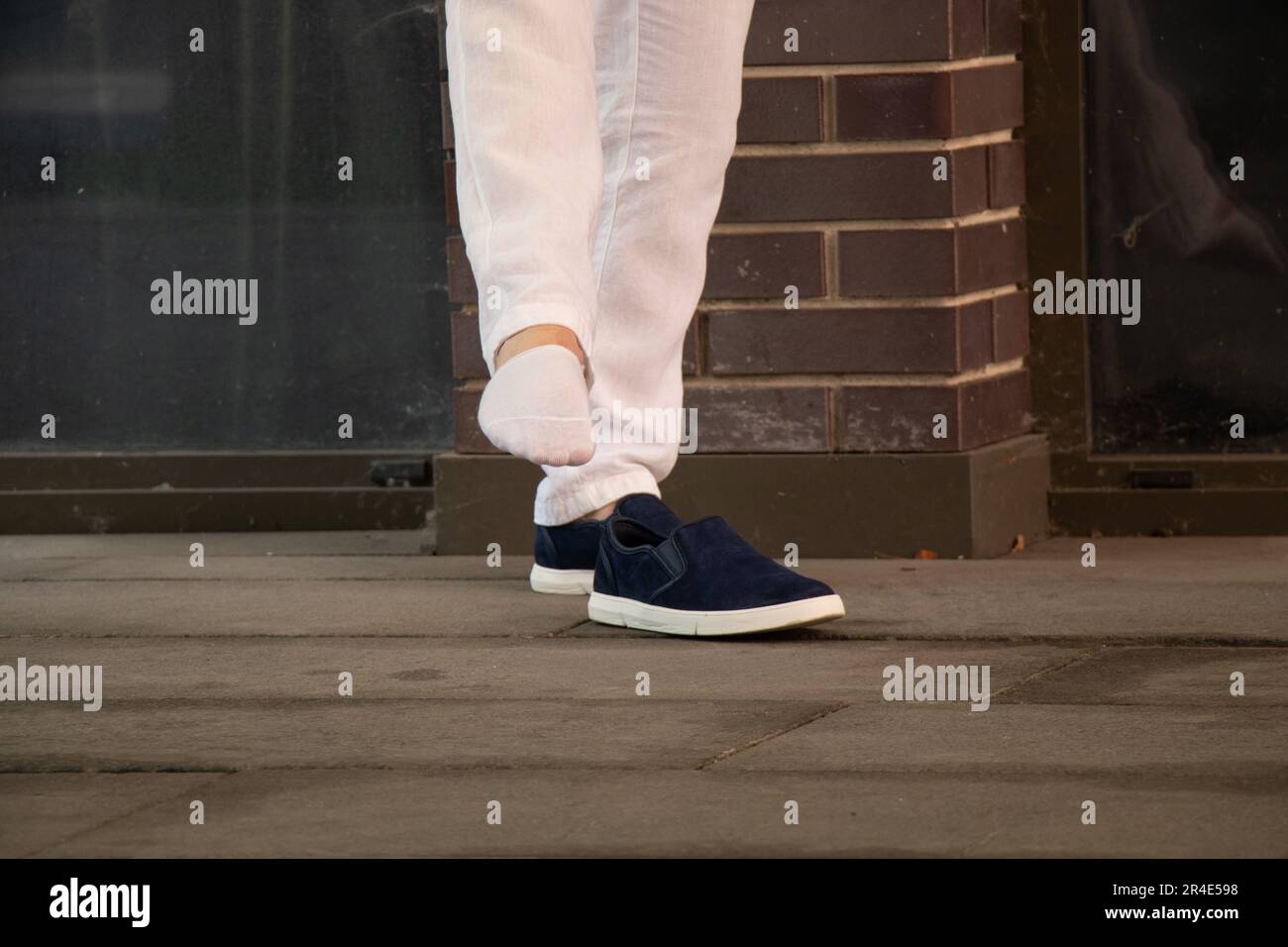 A man puts on short white socks on his feet and next to stand blue sneakers on the street in the city center, fashion and style, legs and socks Stock Photo