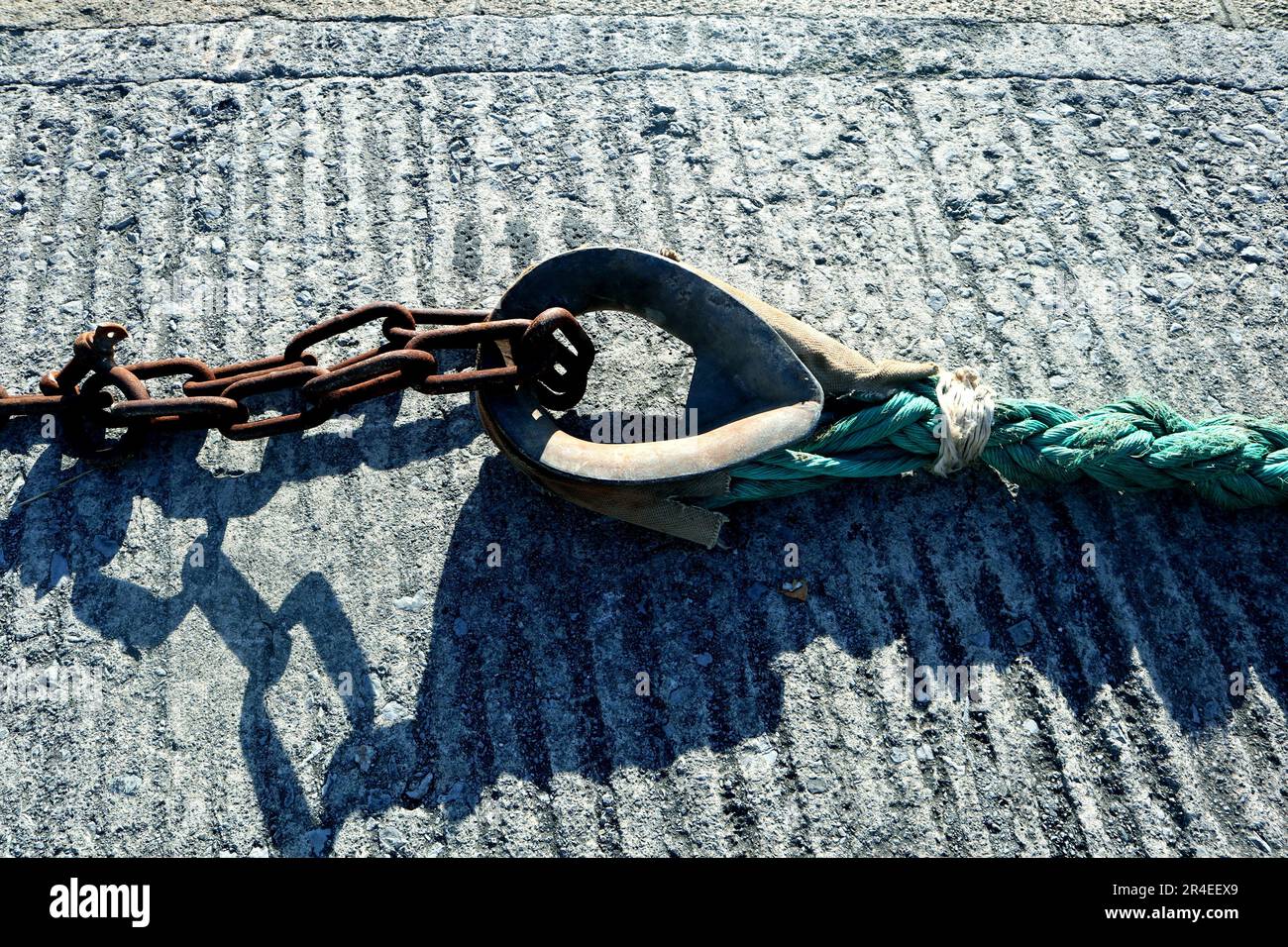A rustic brown rope resting atop a sturdy metal anchor, against a plain sand-colored background Stock Photo