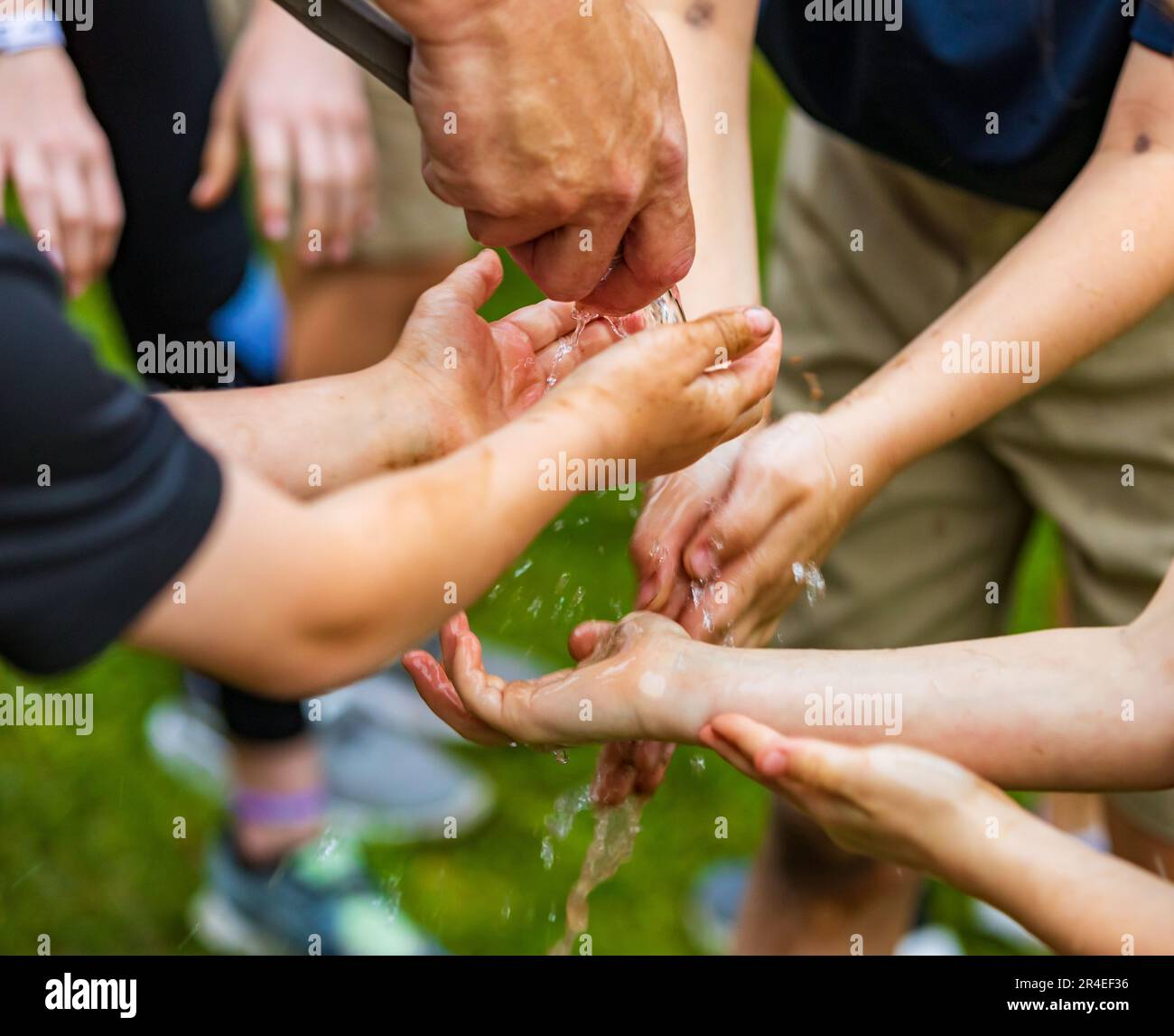 Children outside washing hands with water from garden hose. Stock Photo