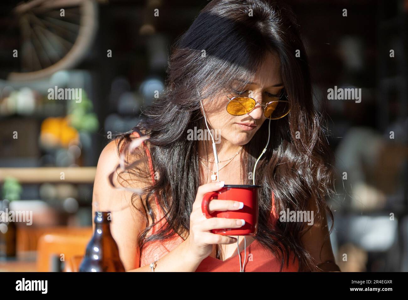 Close-up view of a woman holding a cup of coffee and listening to music with earphones at a coffee shop. Stock Photo