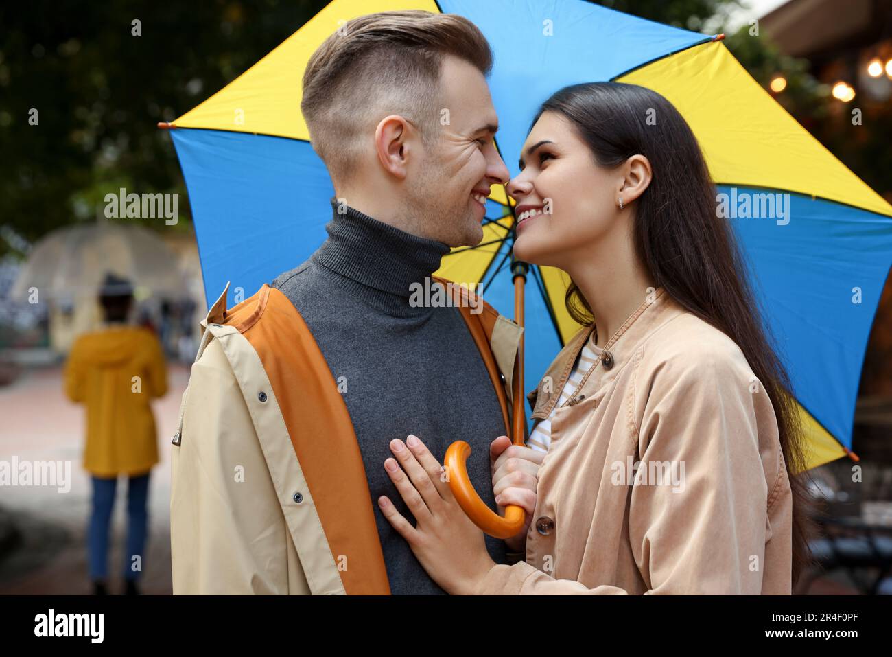 Lovely young couple with umbrella walking under rain on city street ...