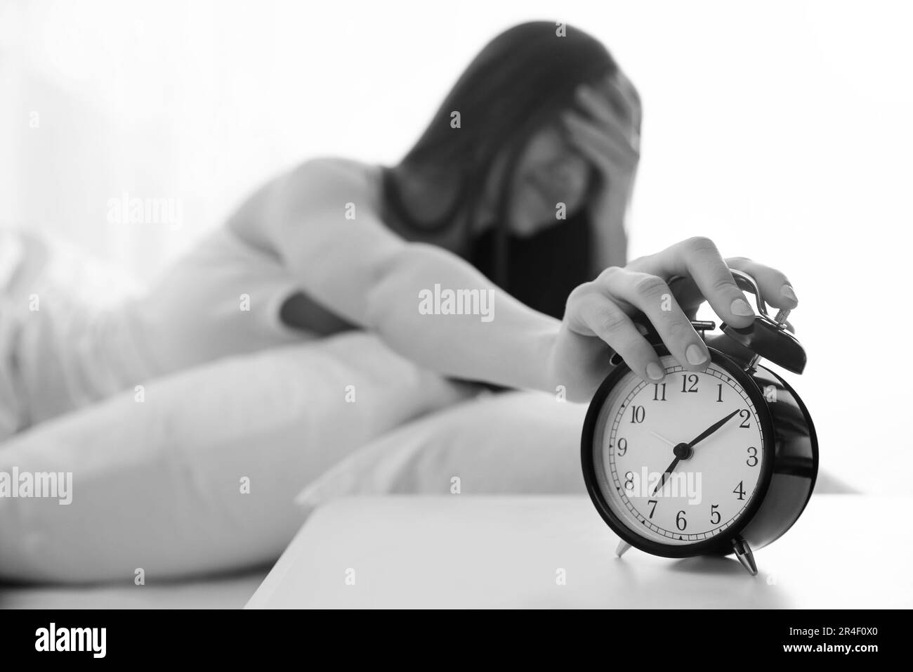 Young woman turning off alarm clock at home in morning, selective focus. Black and white photography Stock Photo