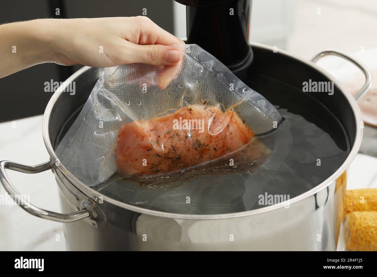 Woman putting vacuum packed meat into pot with sous vide cooker