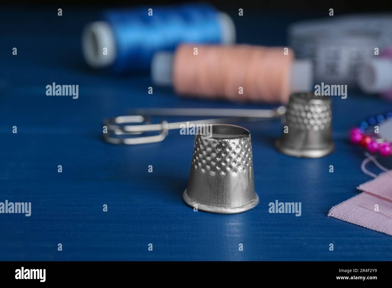 Silver thimble on blue wooden table, space for text. Sewing accessory Stock Photo