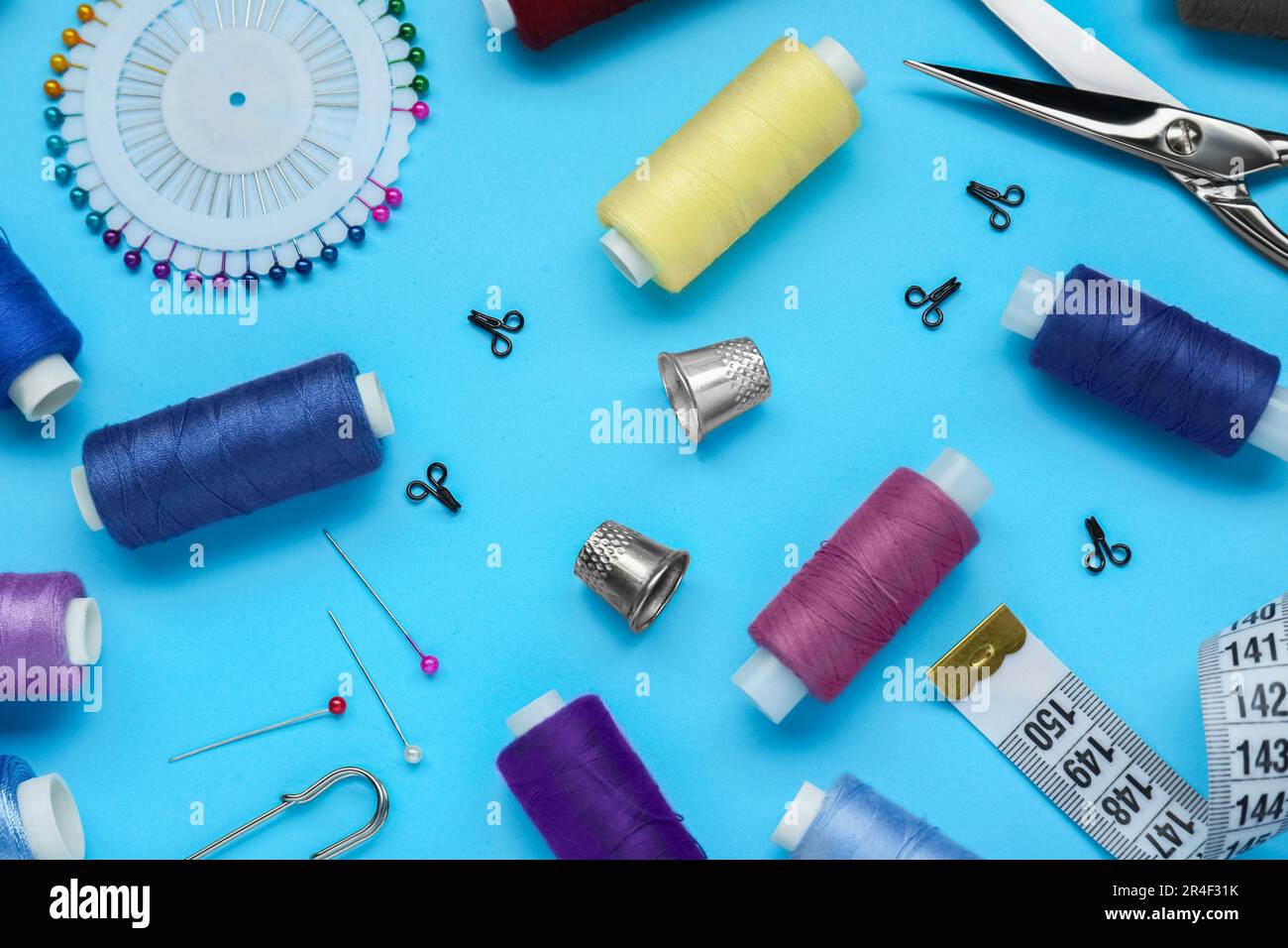 Flat lay composition with thimbles and different sewing tools on light blue background Stock Photo