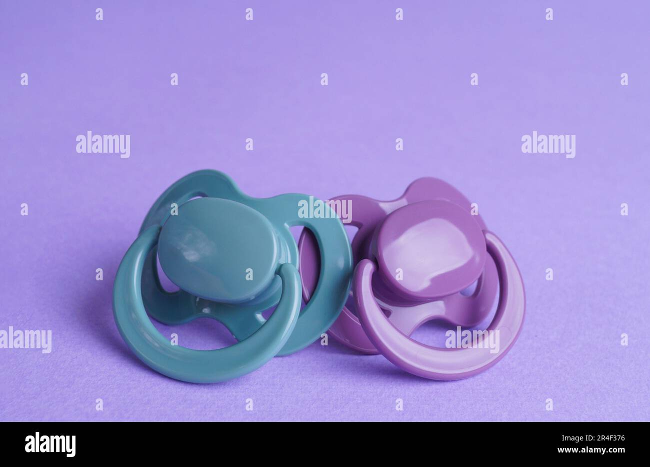 New baby pacifiers on purple background, closeup Stock Photo