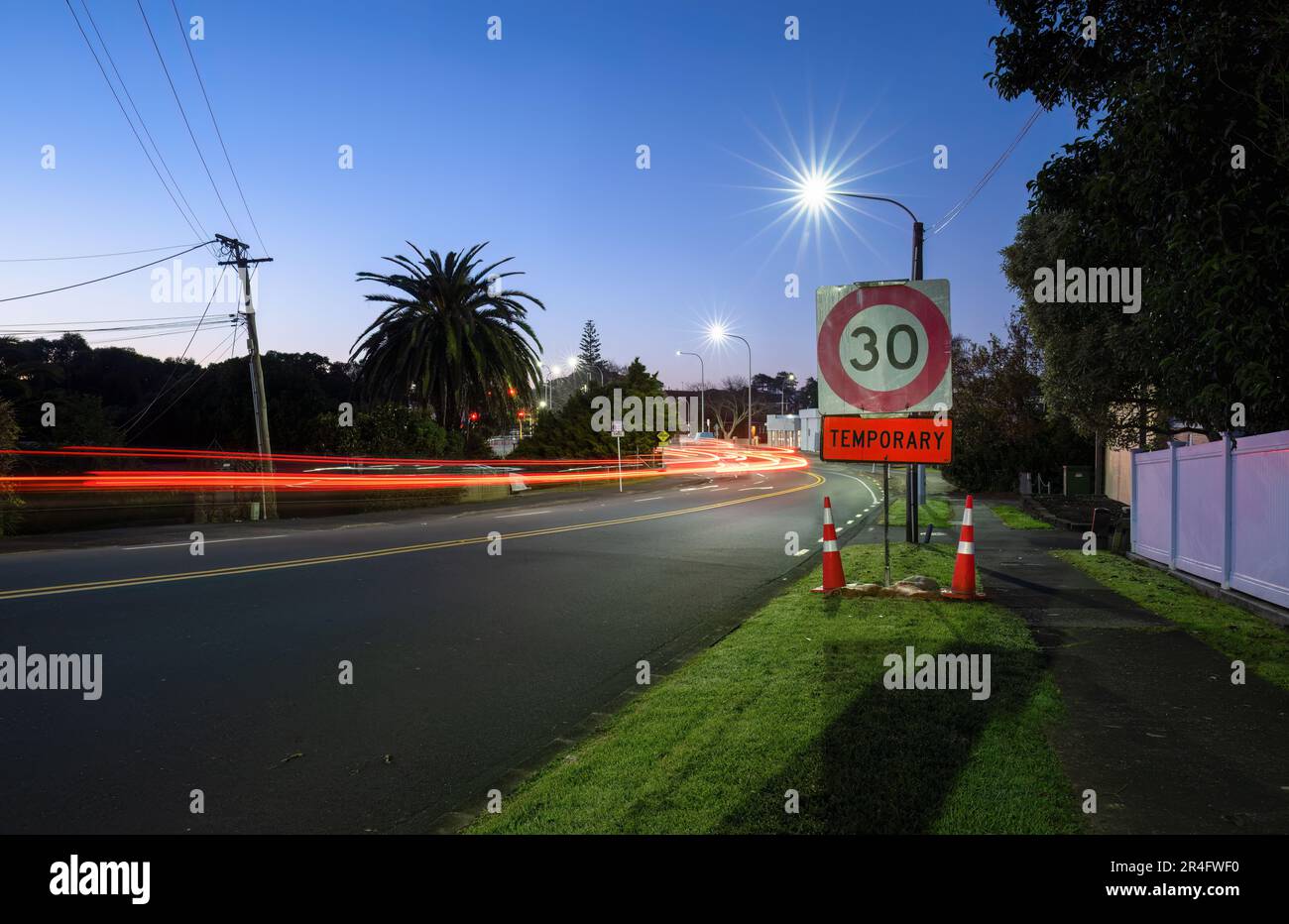 Temporary 30km speed limit sign with traffic cones by the roadside. Car light trails on the road intersection. Auckland. Stock Photo