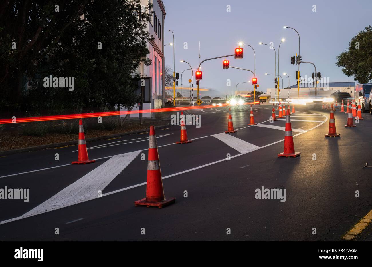 Orange traffic cones lined up on the road. Car light trails on the road intersection. Auckland. Stock Photo