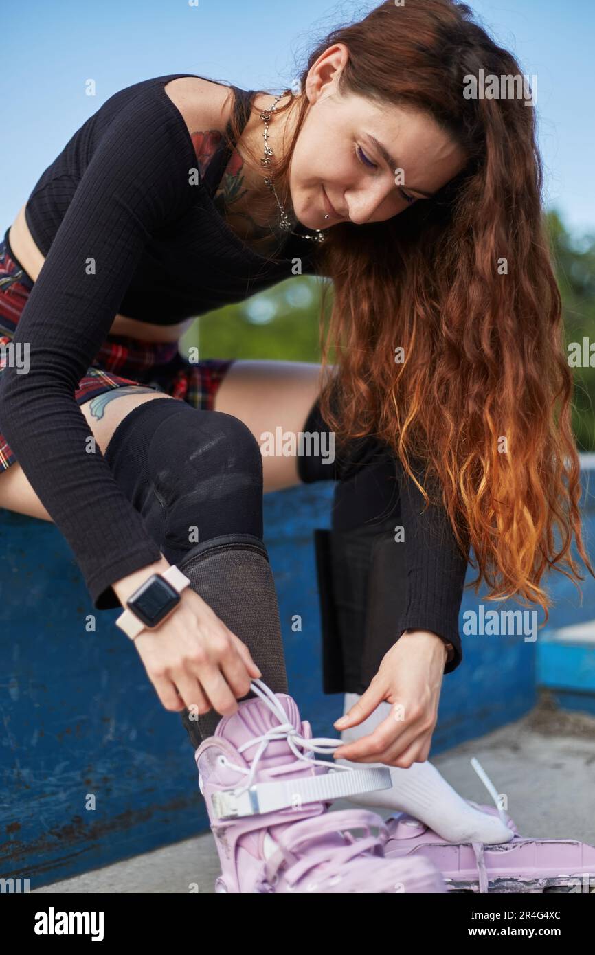 Beautiful young woman putting on inline skates in a skatepark. Cheerful