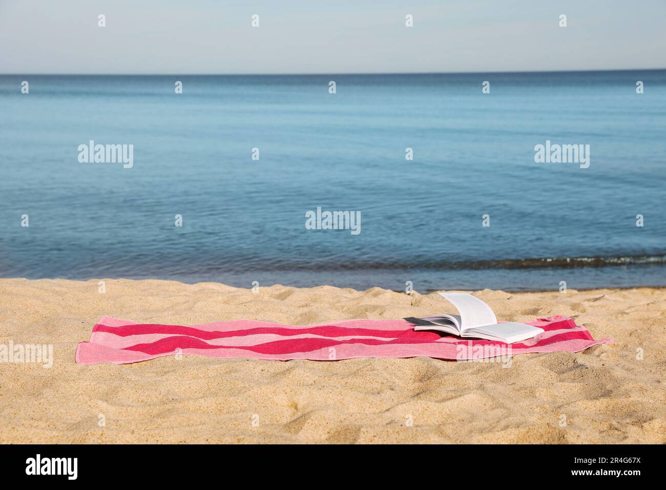 Beach towel and open book on sand near sea, space for text Stock Photo ...