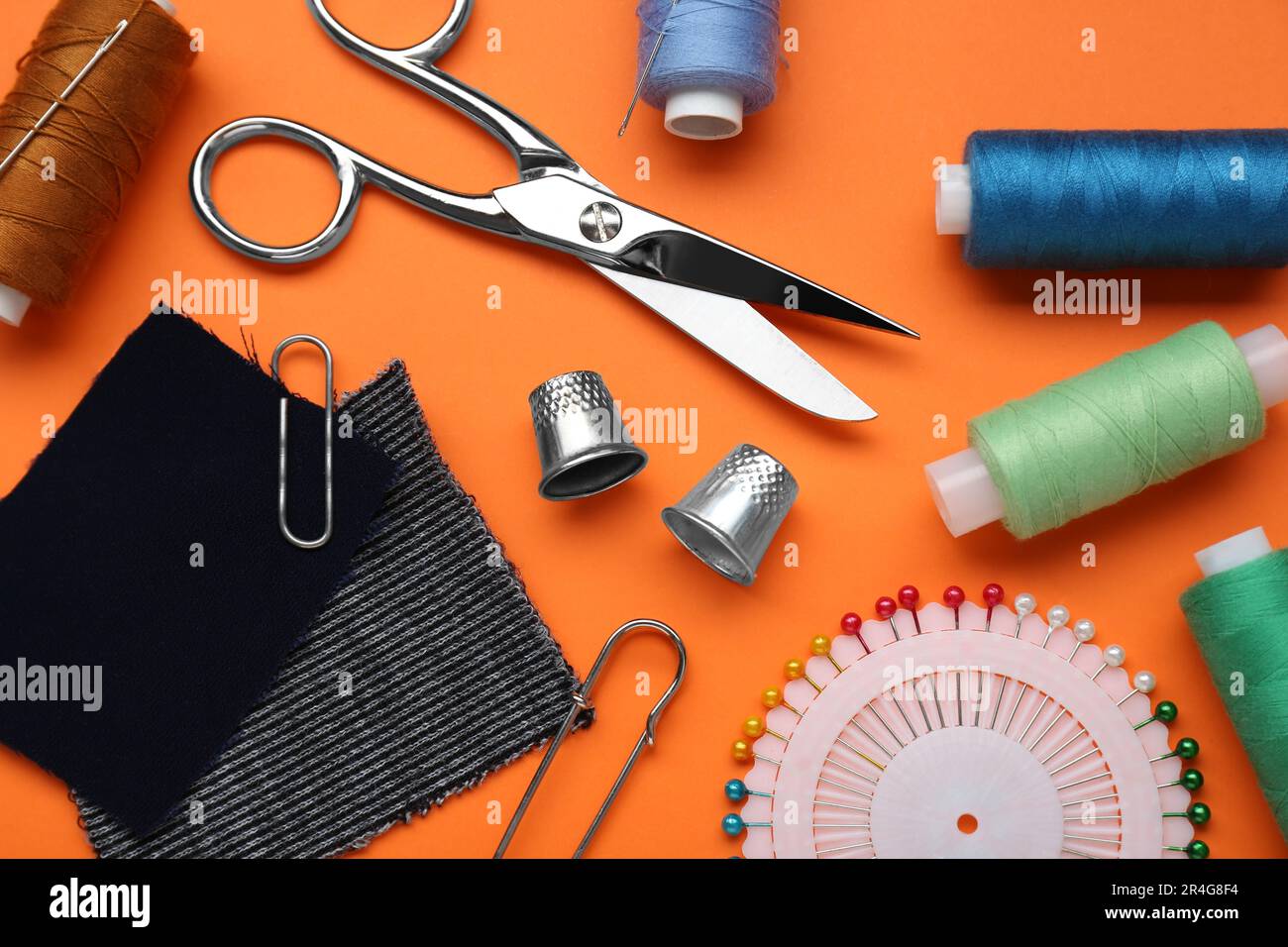 Flat lay composition with thimbles and different sewing tools on orange background Stock Photo