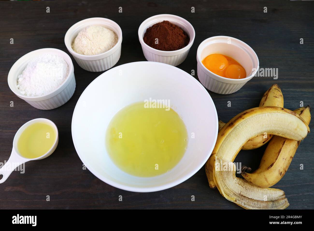 Egg White in a Mixing Bowl Surrounded with Ingredients for Baking Banana Chocolate Cake Stock Photo