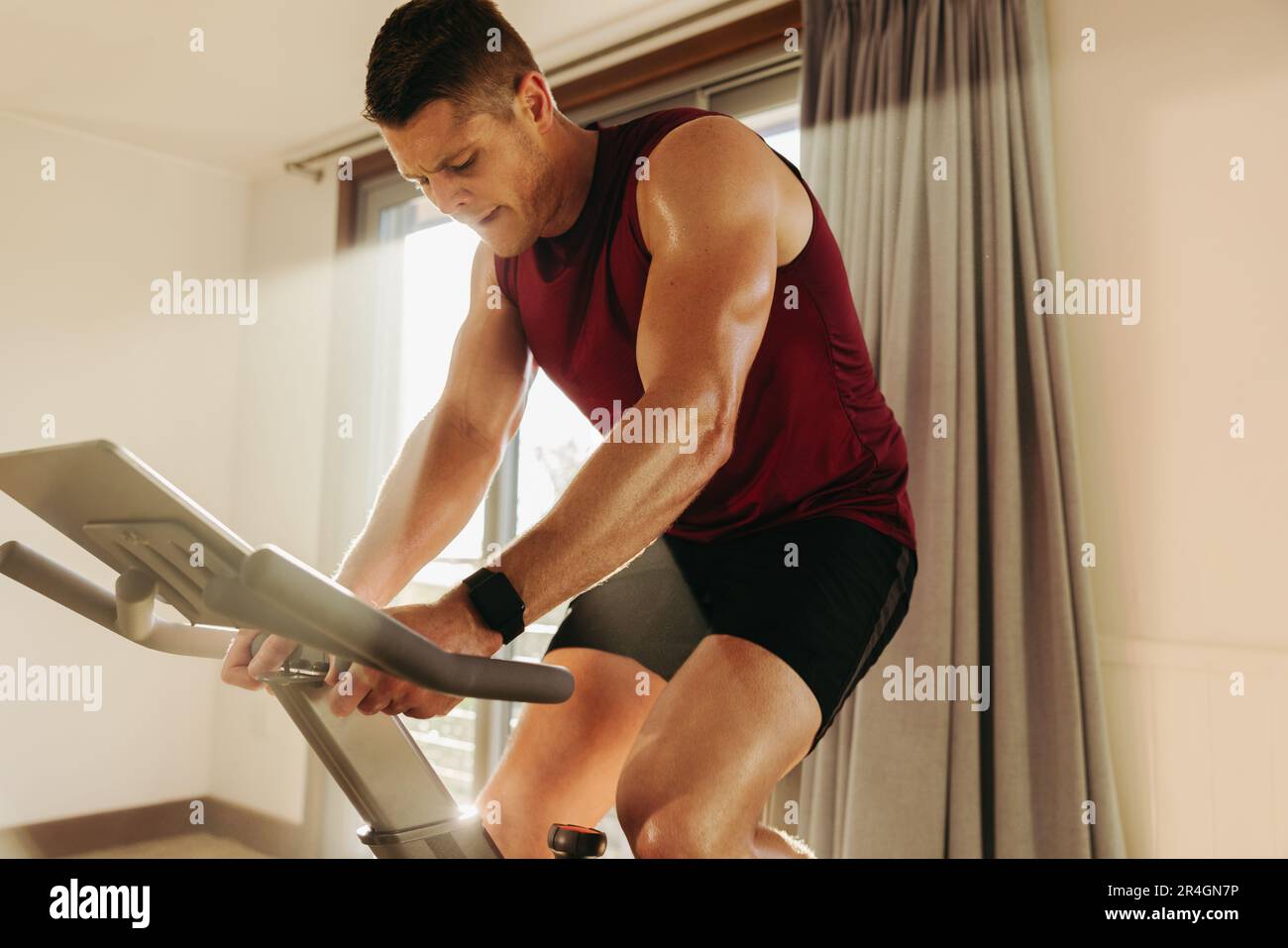 Male athlete using a smart exercise bike to boost his fitness, taking full advantage of fitness technology to stay on top of his game. Young Caucasian Stock Photo