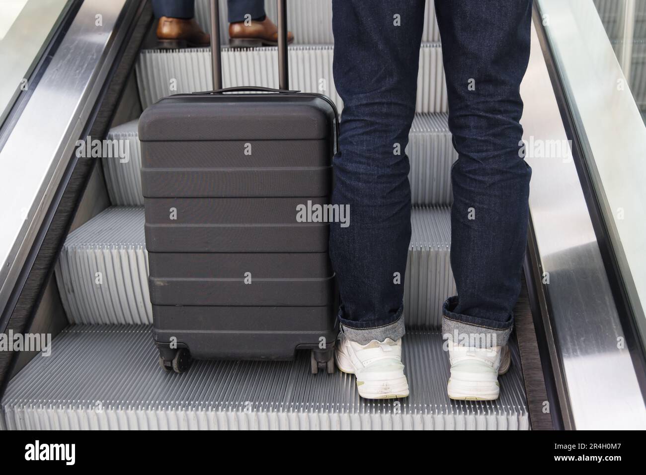 legs of a person with a wheeled suitcase on an escalator Stock Photo