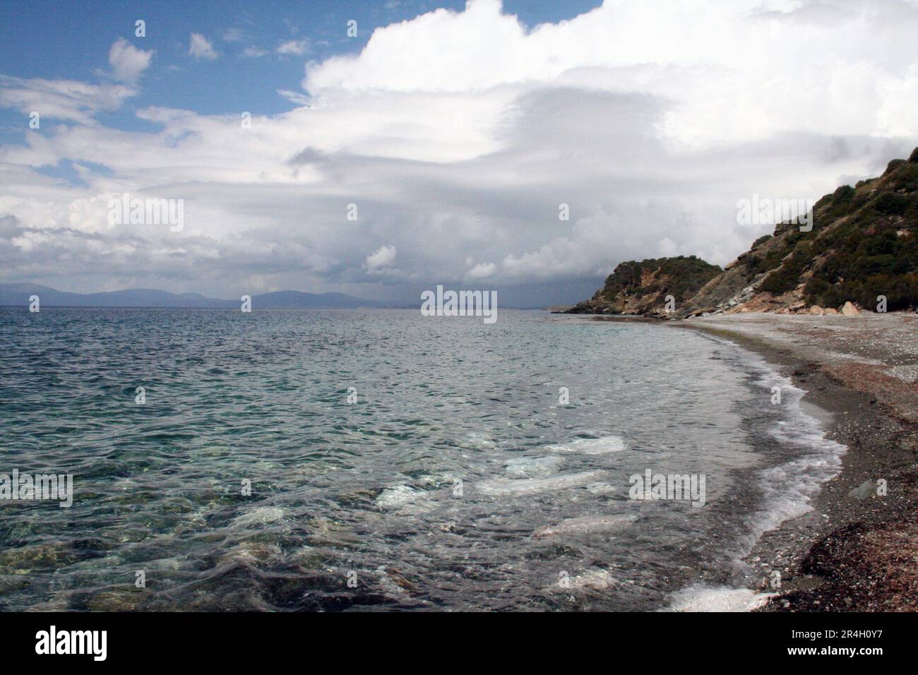 Rocky coast beach island on Aegean Mediterranean Sea cloudy sky reflection on water wave natural coastline seashore panoramic view Stock Photo