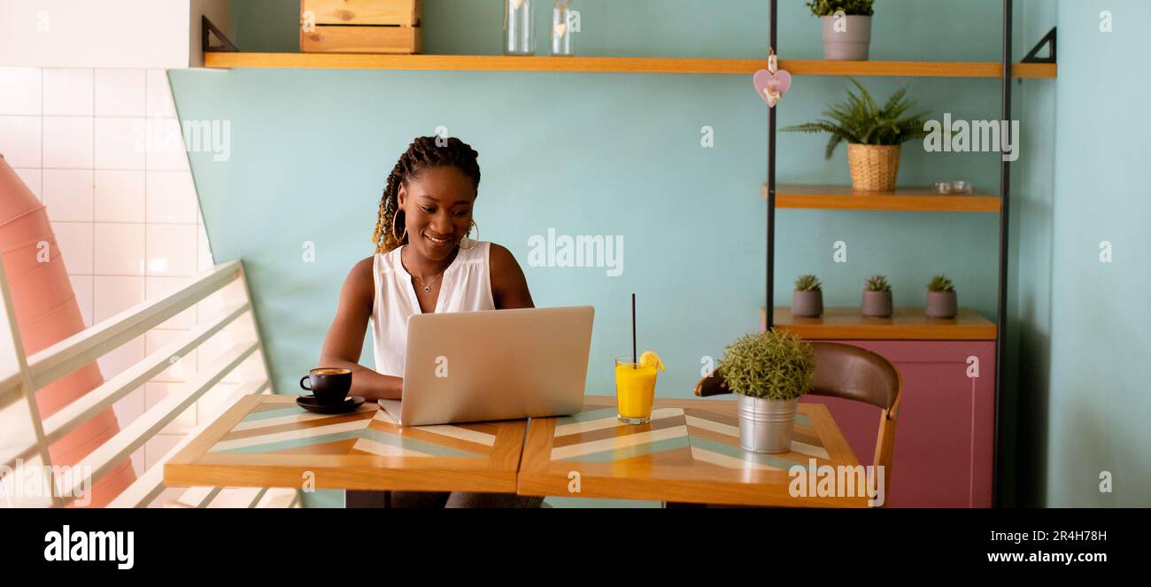 Pretty young black woman drinking coffee while working on laptop in the ...