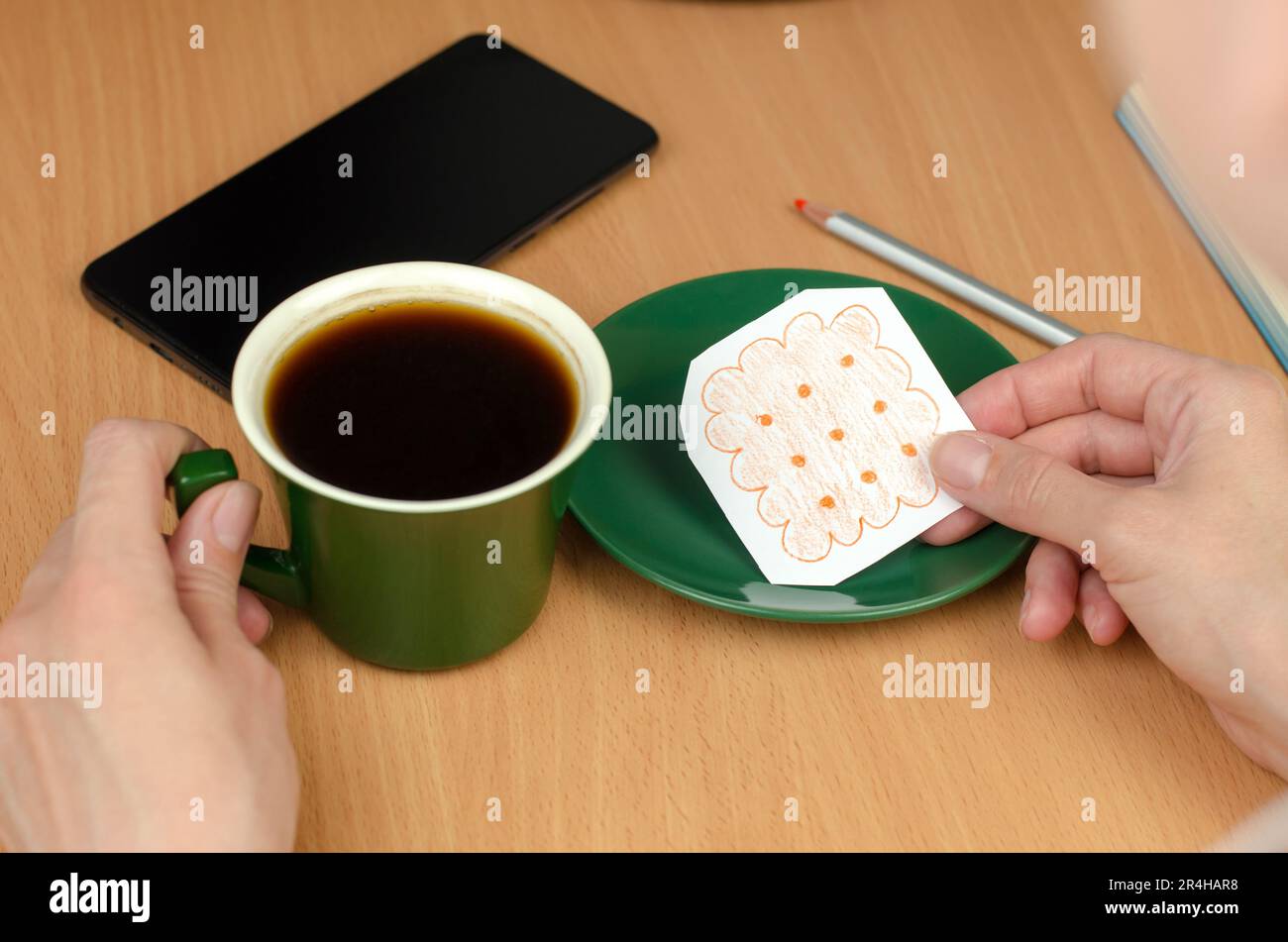 A woman's hand draws cookies. A cup of coffee and a painted cookie on a saucer. Concept without food and money Stock Photo