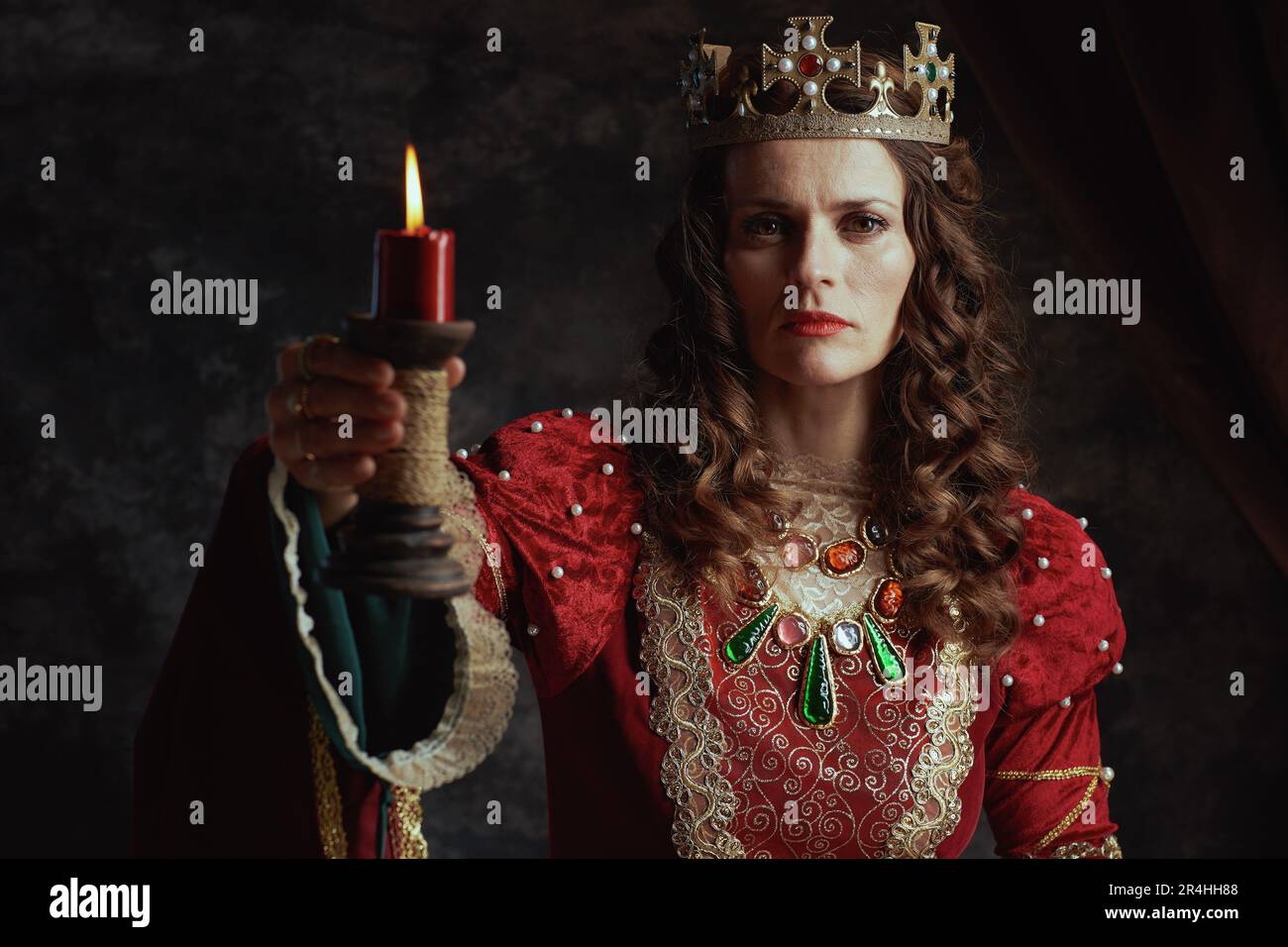 medieval queen in red dress with candle and crown on dark gray ...