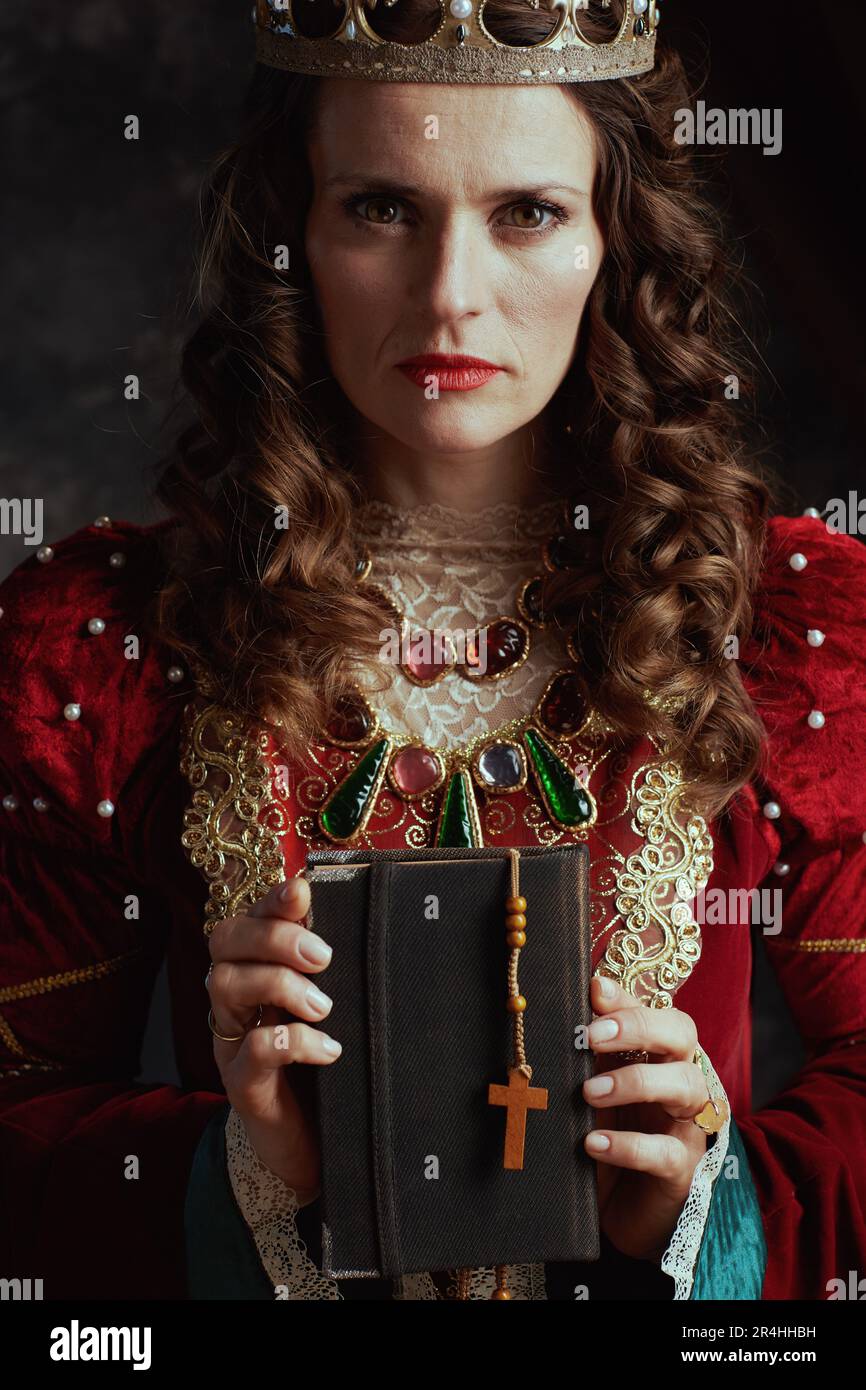 medieval queen in red dress with book, rosary and crown on dark gray ...