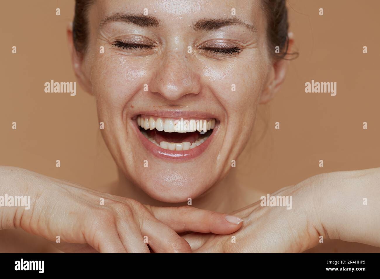 smiling middle aged woman with wet face washing on beige background