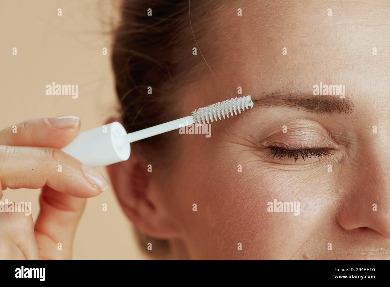Closeup on 40 years old woman with brow brush isolated on beige background. Stock Photo