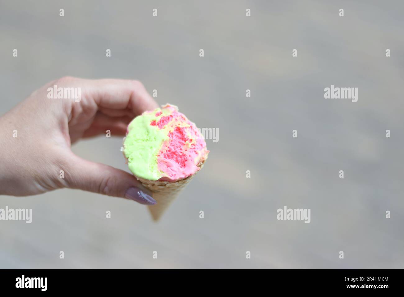 A woman holds an ice cream cone in both hands. Ice cream is bitten. Shot close-up. Stock Photo