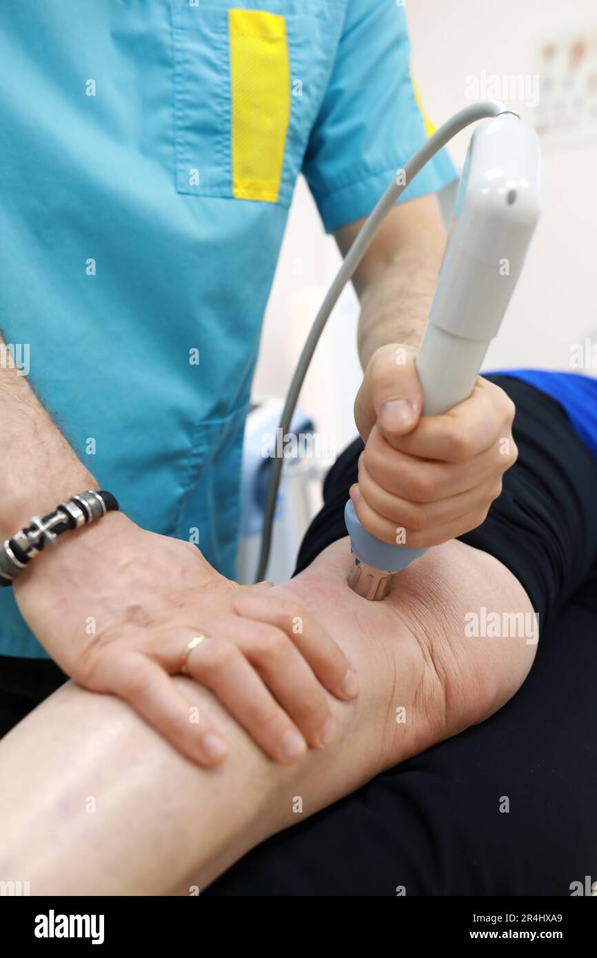 Osteopath treating knee to senior woman with shock wave therapy in clinic Stock Photo