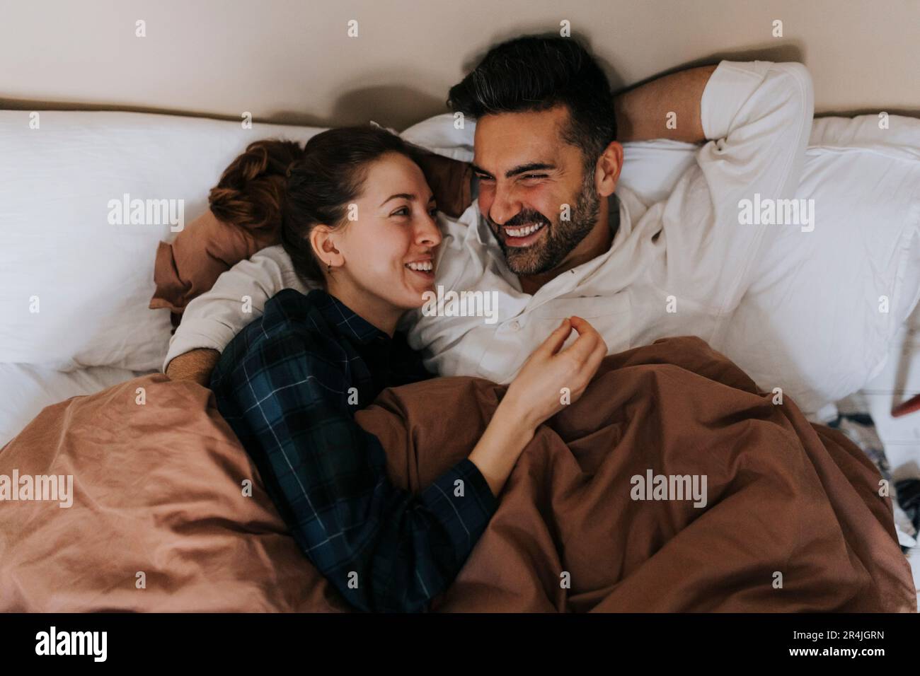 Cheerful non-binary person talking to boyfriend while lying on bed at home Stock Photo