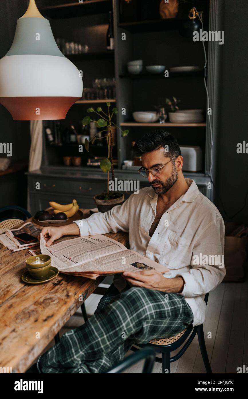 Man reading newspaper while sitting on chair at home Stock Photo