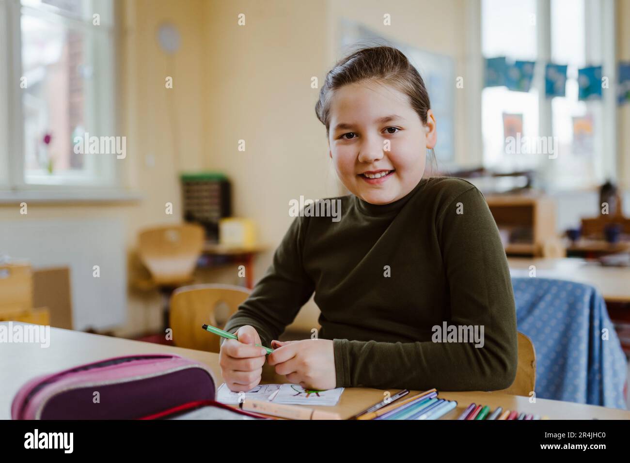 Portrait of smiling female pupil sitting at desk in classroom Stock ...