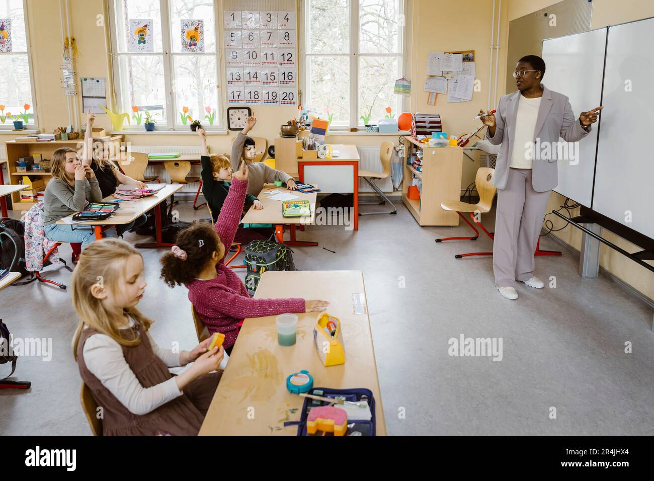 Teacher standing by whiteboard while asking questions to students in classroom Stock Photo