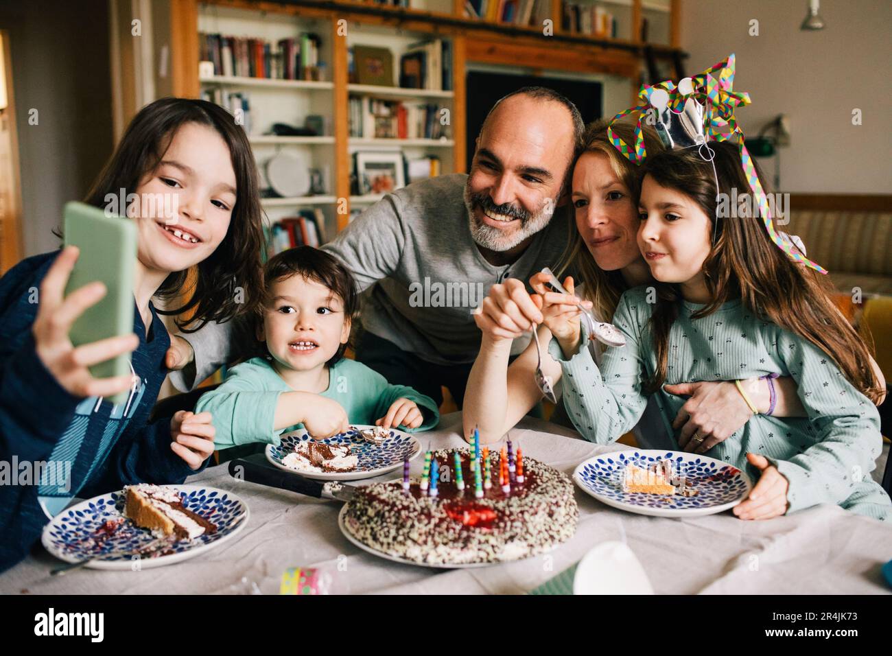 Boy taking selfie with family eating birthday cake while enjoying at home Stock Photo