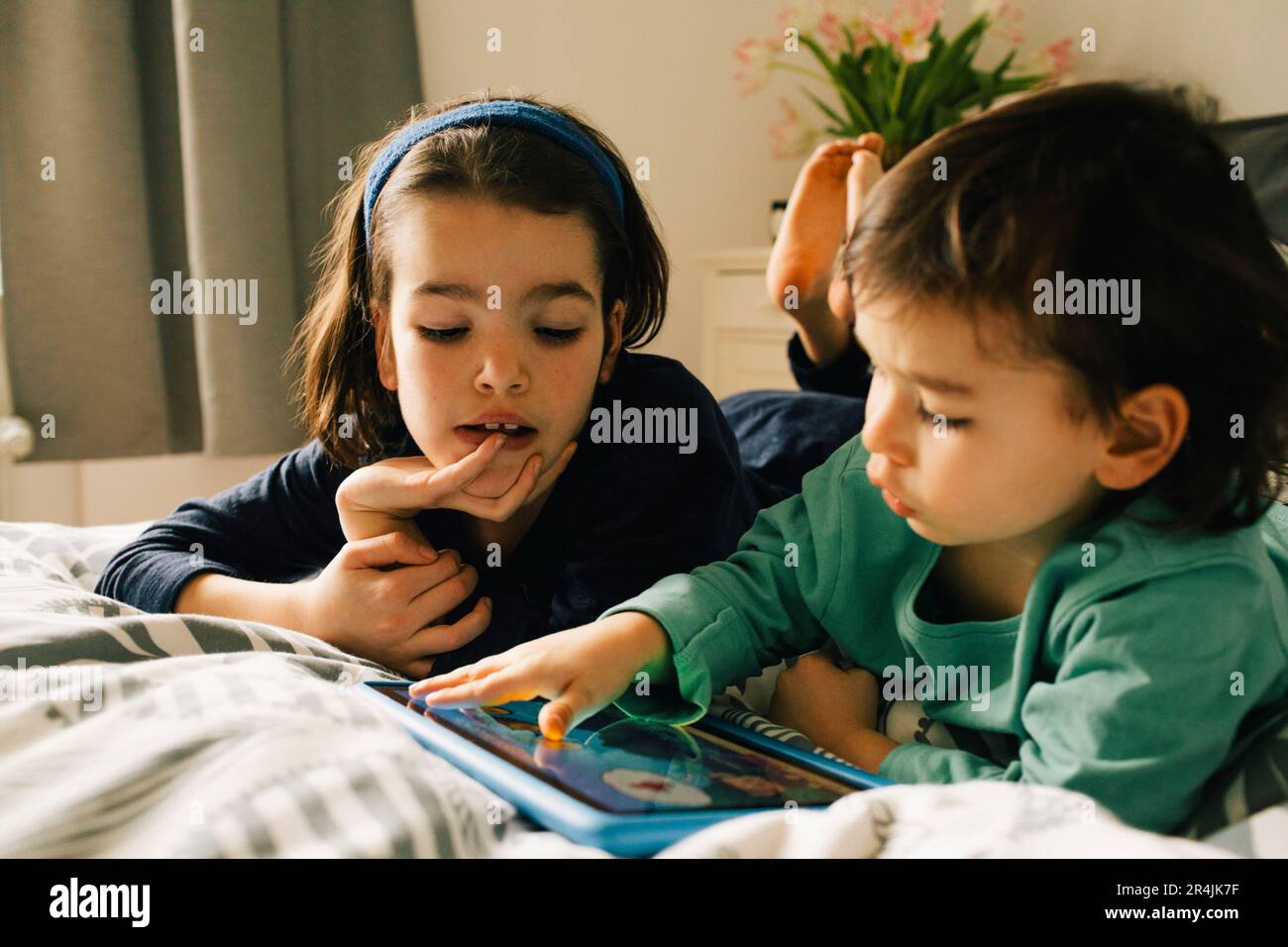 Brothers using digital tablet while lying together on bed at home Stock Photo