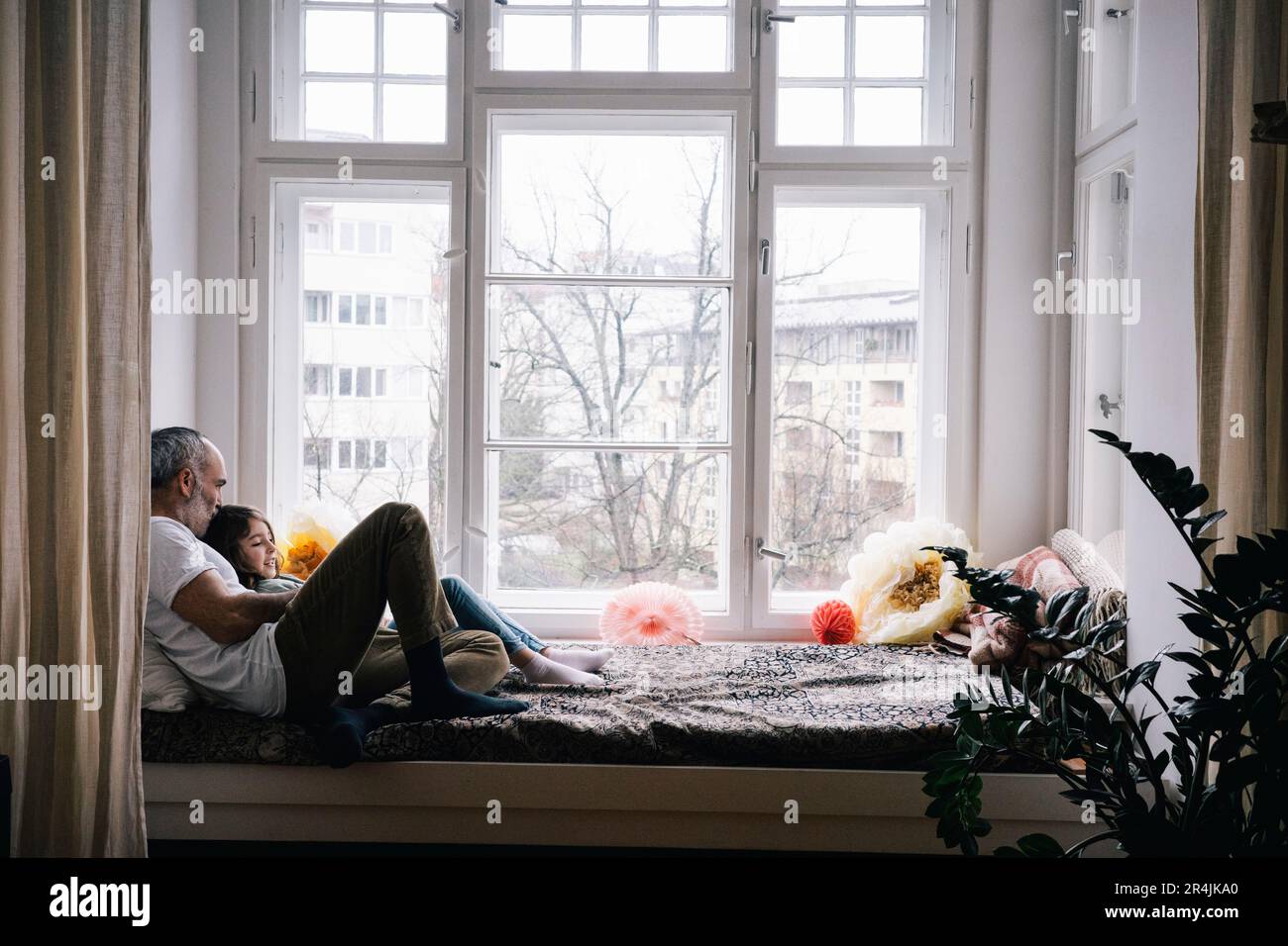 Father and daughter sitting together on alcove window seat at home ...