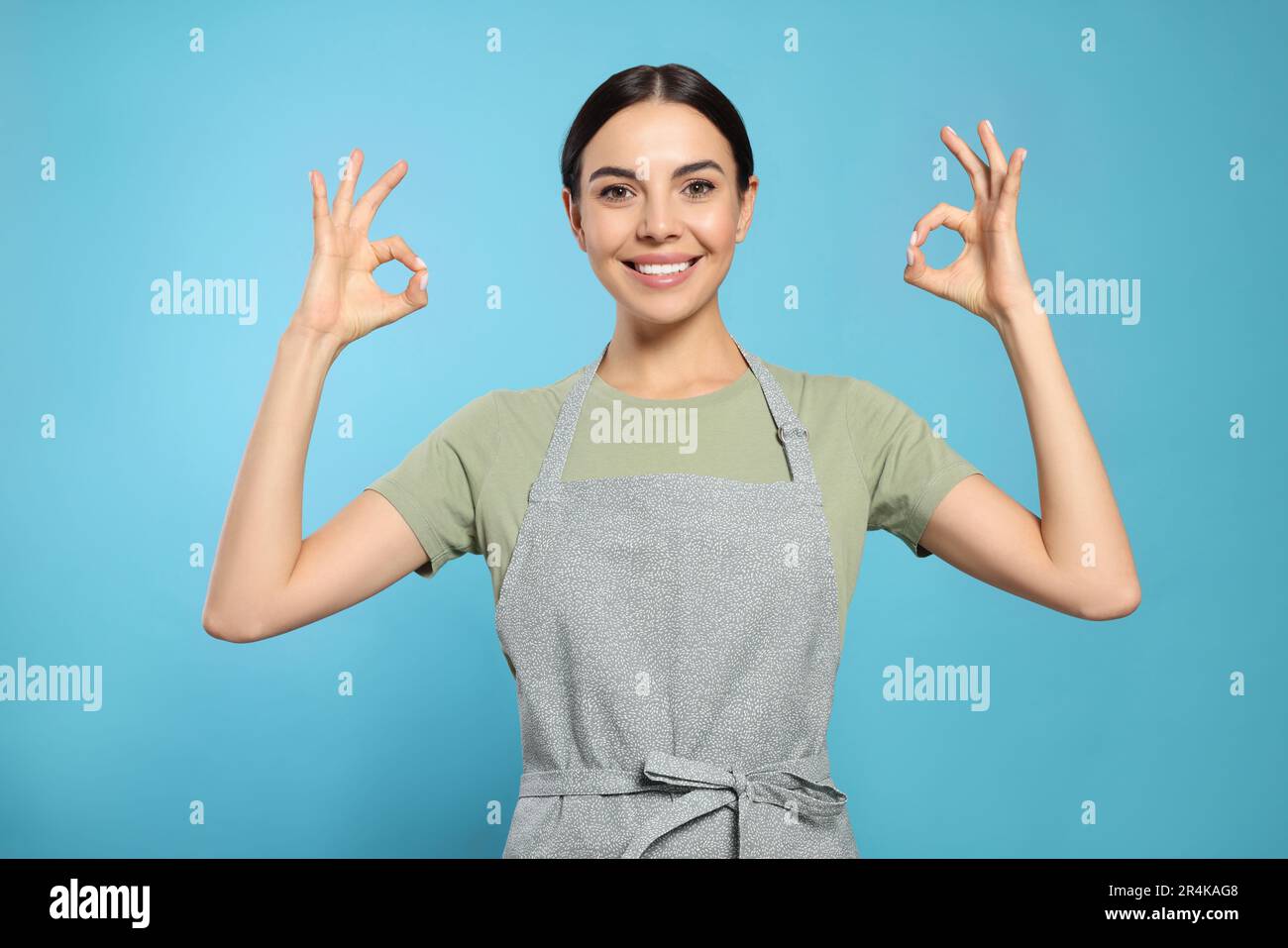 Young woman in grey apron on light blue background Stock Photo - Alamy