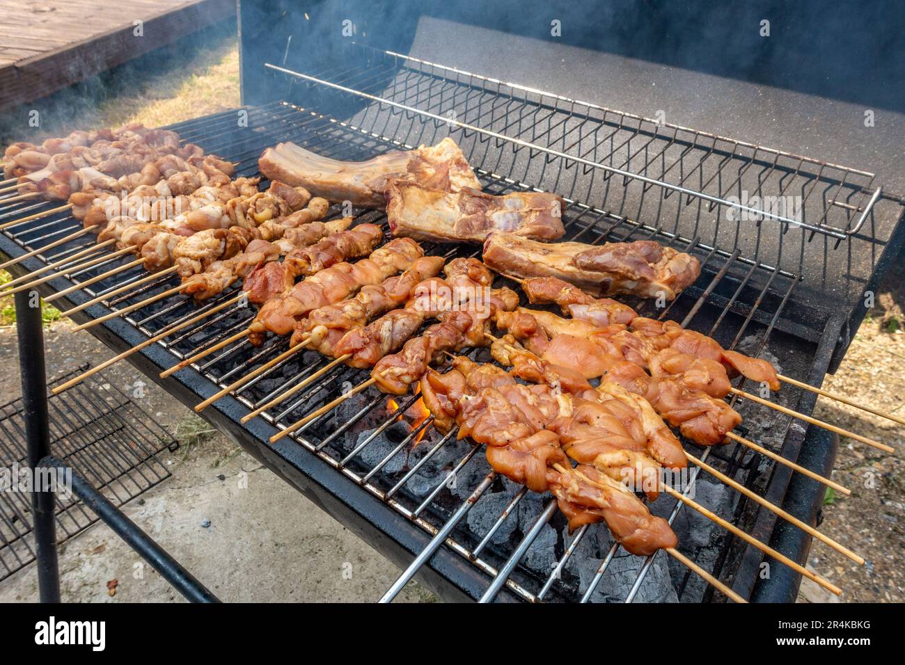 Pork barbecue cooking in a grill. Pork is pushed onto wooden skewers to cook Stock Photo Alamy