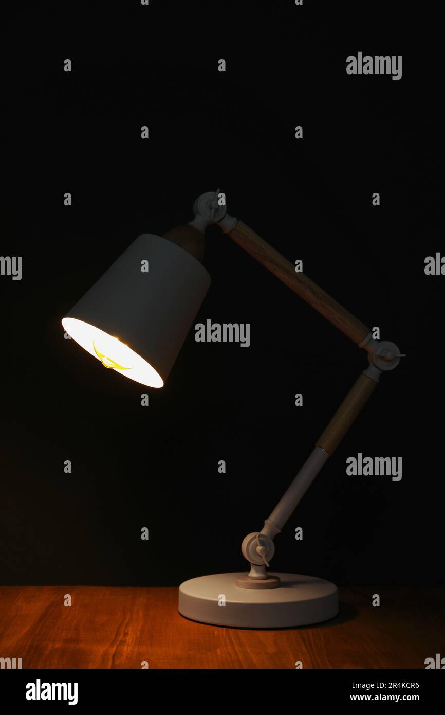 Stylish modern desk lamp on wooden table at night Stock Photo