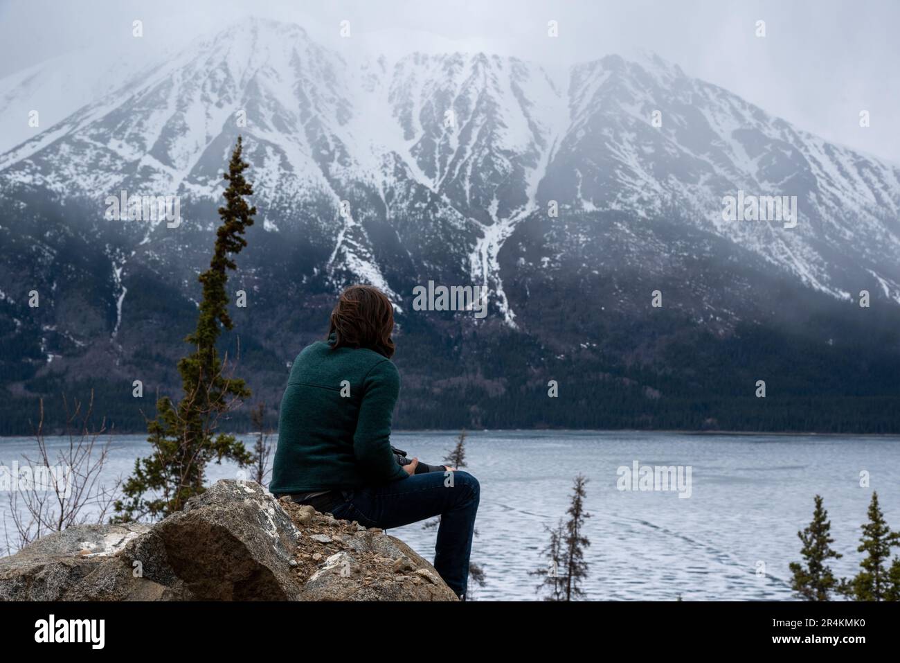 Unique view of a person with reflection in a natural lake with clouds and mountains in background. Awesome perspective of person. Stock Photo