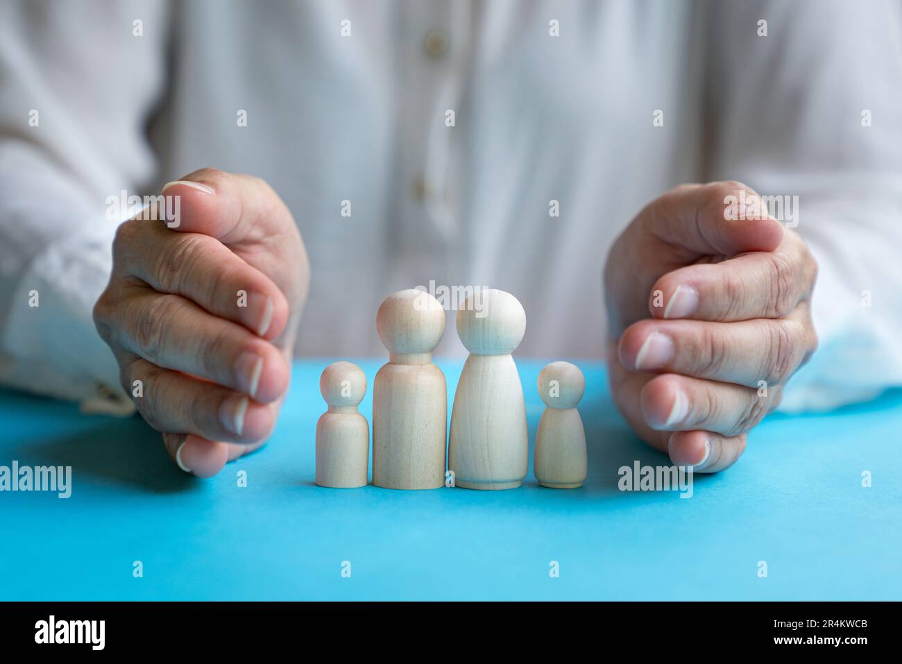 Woman's hands cover over wooden doll family with father, mother, daughter and son. Family care and protection concept. Stock Photo