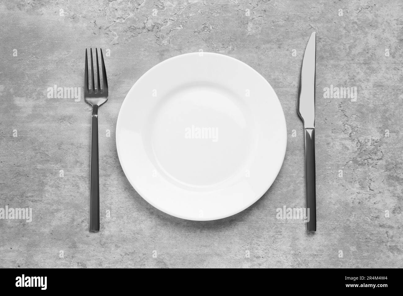 Clean plate and shiny silver cutlery on light grey table, flat lay